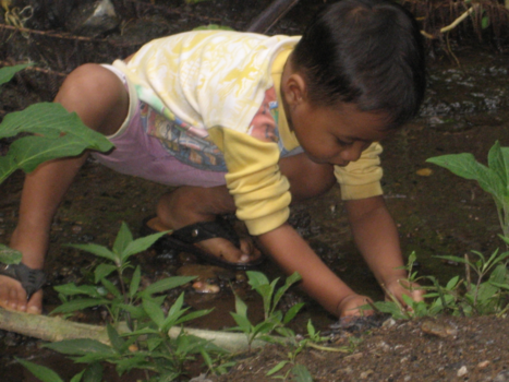 Bali - In zijn eigen wereld spelend aan een riviertje met zeld gemaakt bootje