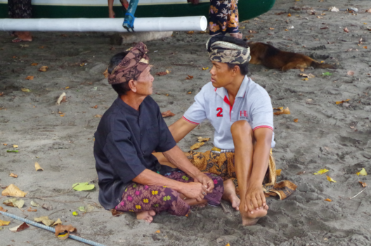 Bali - Twee mannen op het strand van Lovina, Bali (verderop een crematie)